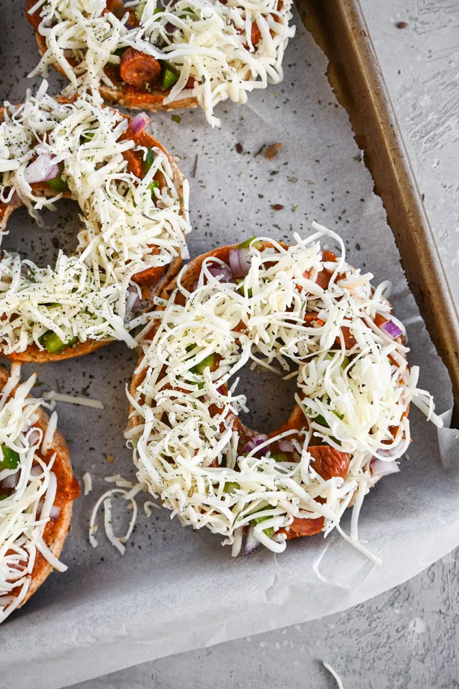 bagel pizza assembled and ready for freezer on a sheet pan